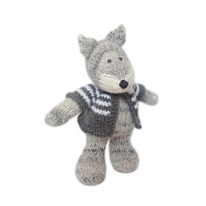 Può includere: Un peluche fatto a mano a forma di lupo grigio con un naso nero e un maglione a righe grigie e bianche. Il lupo ha la faccia e le orecchie grigio chiaro ed è in piedi con le braccia tese.