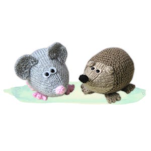 May include: Two knitted animal toys: a grey mouse with pink details and a brown hedgehog. The mouse has large ears and googly eyes. The hedgehog has a black nose and small, round eyes. Both are on a light green surface.