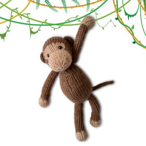 Könnte beinhalten: Ein braunes, gestricktes Affenspielzeug mit einem langen Schwanz, das an einer Rebe hängt. Der Affe hat ein hellbraunes Gesicht mit schwarzen Augen und einer kleinen, rosafarbenen Nase.