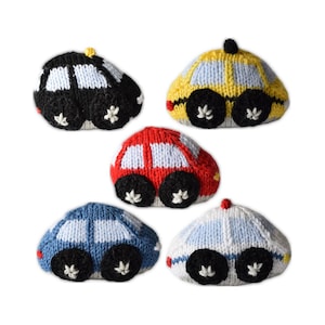May include: Five hand-knitted toy cars in various colors: black, yellow, red, blue, and white. Each car features black wheels and white floral accents. The cars are designed with a rounded shape and a knitted texture.