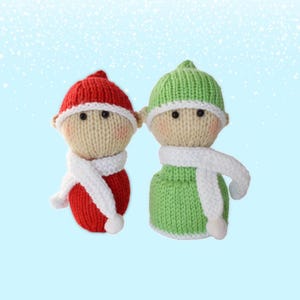 May include: Two knitted dolls, one in red with a white scarf and hat trim, the other in green with a white scarf and hat trim. Both dolls have beige faces, rosy cheeks, and black eyes. The background is a light blue with white specks.
