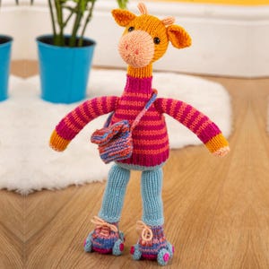 Op de afbeelding: Een handgemaakte gebreide giraffepop met oranje, roze en blauwe accenten. De giraffe draagt een gestreepte trui, een blauwe broek en bijpassende schoenen. Het heeft een kleine tas en is een grillig speelgoed.