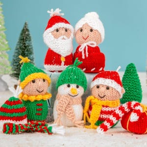 May include: A selection of knitted Christmas decorations featuring Santa Claus, Mrs. Claus, an elf, a snowman, and a child in a Santa hat. The ornaments are in red, green, white, and yellow, with smiling faces and festive details.
