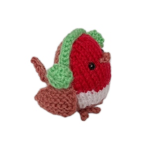 May include: A handmade knitted robin bird with a red body, white chest, and brown wings. The bird wears green earmuffs. This charming, festive decoration is perfect for holiday decor or as a unique gift.