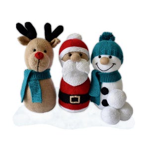 May include: A trio of knitted Christmas decorations: a reindeer, Santa Claus, and a snowman. The reindeer is beige with black antlers and a red nose, wearing a teal scarf. Santa wears a red suit with a white beard. The snowman has a teal hat and scarf.
