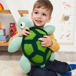 May include: A child holds a knitted green and light blue turtle toy. The turtle has a green shell with a pattern of hexagons. The child is wearing a yellow shirt.