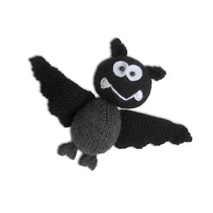 May include: A handmade crochet bat toy featuring a dark gray rounded body, black textured wings, and a black head. The face includes two white felt circles with black bead eyes, and a white stitched mouth with two small white felt fangs.