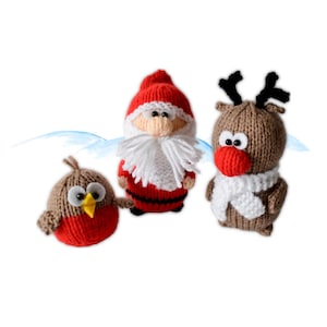 Könnte beinhalten: Drei gestrickte Weihnachtsdekorationen: ein Weihnachtsmann, ein Rentier und ein Rotkehlchen. Der Weihnachtsmann hat einen roten Hut und Anzug mit weißem Bart. Das Rentier hat ein Geweih und eine rote Nase. Das Rotkehlchen ist braun und rot.