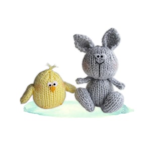 May include: Two knitted stuffed animals: a yellow chick and a gray bunny. The chick has a yellow body, wings, and a small orange beak. The bunny has long ears and a smiling face. Both are sitting on a light blue surface.