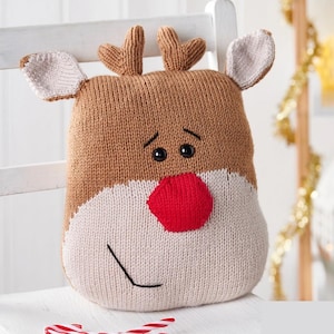 Puede incluir: Un cojín de reno tejido con cabeza marrón, orejas beige y nariz roja. El cojín tiene ojos negros y una sonrisa cosida. Ideal para la decoración navideña.