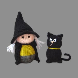 Puede incluir: Figuras de Halloween tejidas a mano. Una muñeca de bruja con sombrero negro, abrigo y vestido amarillo y gris, y un gato negro con collar amarillo. La bruja tiene pelo blanco y cara rosa. El gato tiene ojos blancos y nariz blanca.