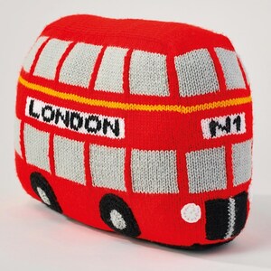May include: A red, knitted, soft-sculpture London double-decker bus with grey windows, black wheels, and white headlights. The front features the text LONDON and N1 in black lettering on a white background, with a thin yellow horizontal stripe.