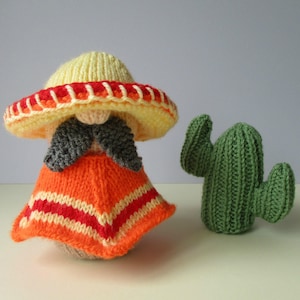 Może przedstawiać: Dzianinowa lalka w żółtym sombrero z czerwonymi i białymi paskami i pomarańczowym ponczo z czerwonymi i białymi paskami. Lalka ma szary wąs i brodę. W tle znajduje się zielony dzianinowy kaktus.