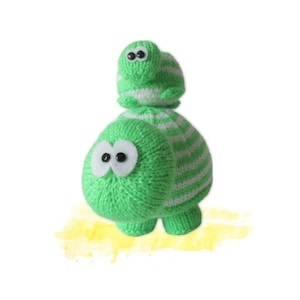 May include: A small knitted creature with a larger knitted creature perched on top. Both are crafted from bright green and white striped yarn. Each figure features large white felt eye patches with small black plastic pupils, giving them a wide-eyed appearance.