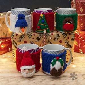 May include: A selection of ceramic mugs with knitted festive cosies. Designs include a snowman, Christmas tree, robin, Santa Claus, and a Christmas pudding. The mugs are displayed on a wooden surface, perfect for the holiday season.