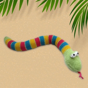 Op de afbeelding: Een gebreide speelgoed slang met een groene kop en een gestreept lichaam. De slang is geel, blauw en roze. De slang ligt op een bruine ondergrond.
