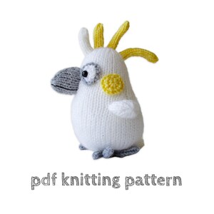 May include: A white knitted cockatoo toy with a grey beak, yellow crest feathers, and a yellow cheek patch. The toy has black button eyes and small grey feet. Below the toy, the text reads pdf knitting pattern in a simple grey font.