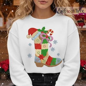May include: White sweatshirt featuring a colorful Christmas boot design. The boot is decorated with a Santa hat, holly, candy cane, and snowflakes. The design incorporates red, green, blue, and tan colors.