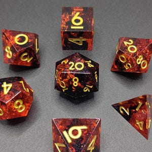 Peut inclure: Ensemble de sept dés polyédriques rouges et noirs avec des chiffres dorés. Ces dés sont destinés aux jeux de rôle sur table. Ils sont fabriqués dans un matériau translucide à l'aspect tacheté et flamboyant.