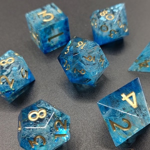 May include: Set of seven polyhedral dice with a blue and white marbled effect, and gold numbering. The dice are for tabletop games and include a D4, D6, D8, D10, D12, D20, and a percentile die.