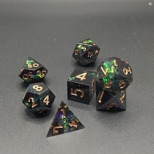 May include: A set of seven polyhedral dice made of black resin with embedded iridescent green and blue foil flakes. Each die features engraved numbers filled with a metallic copper finish, including a d20, d12, d10, d8, d6, and d4.