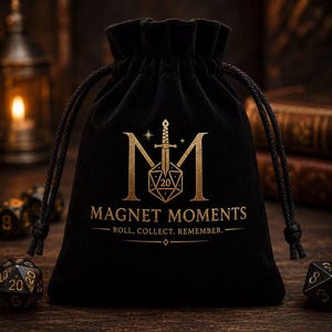 May include: A black velvet drawstring pouch featuring a gold-colored logo with a sword, a twenty-sided die, and the text MAGNET MOMENTS ROLL. COLLECT. REMEMBER. The bag is cinched at the top with black cords and sits on a dark wooden surface.