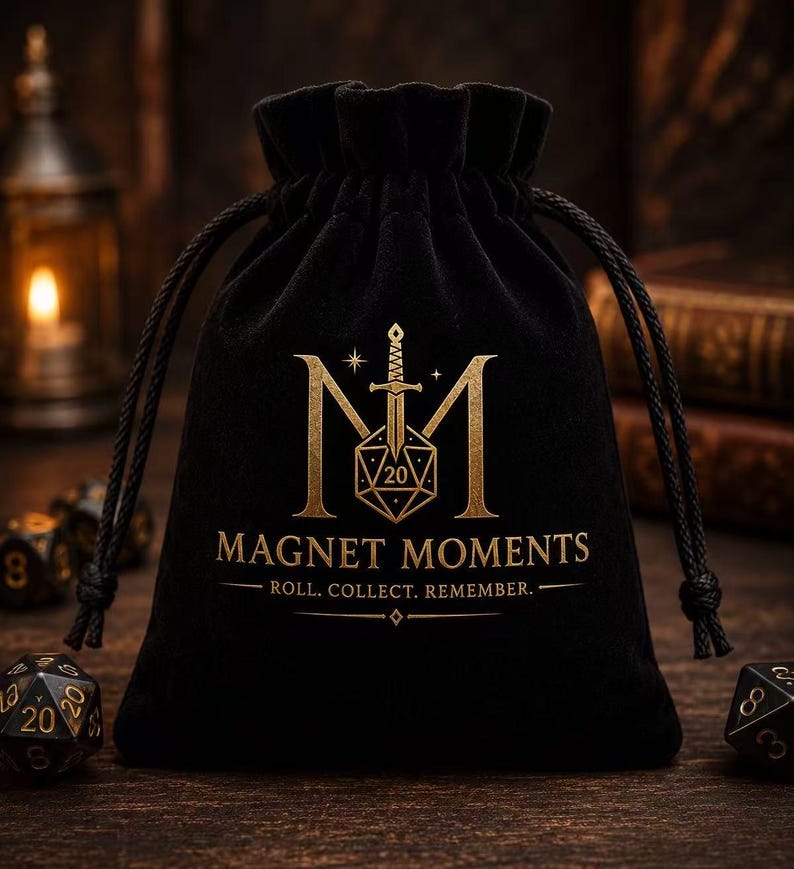 May include: A black velvet drawstring pouch featuring a gold-colored logo with a sword, a twenty-sided die, and the text MAGNET MOMENTS ROLL. COLLECT. REMEMBER. The bag is cinched at the top with black cords and sits on a dark wooden surface.
