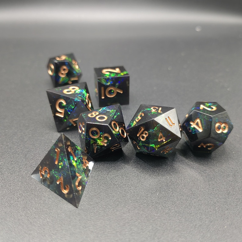 May include: A set of seven polyhedral dice made of black resin with embedded iridescent green and blue foil flakes. Each die features engraved numbers filled with a metallic copper finish, including a d20, d12, d10, d8, d6, d4, and a percentile die.