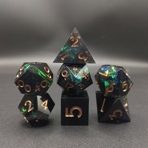 May include: A set of seven polyhedral dice featuring a black base with iridescent green and blue inclusions. Each die has engraved numbers filled with a metallic copper color. The set includes a d4, d6, d8, d10, d12, d20, and a percentile die.
