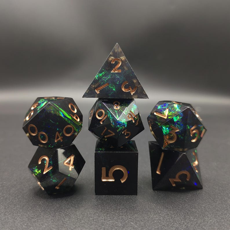 May include: A set of seven polyhedral dice featuring a black base with iridescent green and blue inclusions. Each die has engraved numbers filled with a metallic copper color. The set includes a d4, d6, d8, d10, d12, d20, and a percentile die.