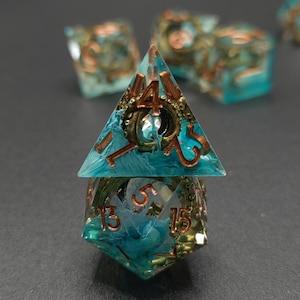 Puede incluir: Un juego de dados poli&eacute;dricos con est&eacute;tica steampunk. Los dados son transparentes con una combinaci&oacute;n de colores turquesa y cobre. Los n&uacute;meros son de color cobre y los dados tienen engranajes y otros detalles mec&aacute;nicos en su interior.