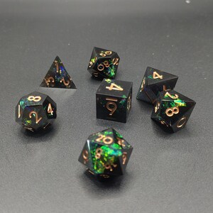 May include: A set of seven polyhedral dice featuring a black base with embedded iridescent green and blue foil flakes. Each die has engraved numbers filled with a metallic copper color, including a d4, d6, d8, d10, d12, d20, and a percentile die.