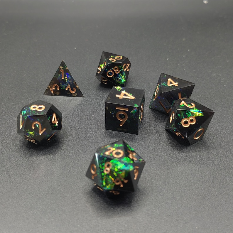 May include: A set of seven polyhedral dice featuring a black base with embedded iridescent green and blue foil flakes. Each die has engraved numbers filled with a metallic copper color, including a d4, d6, d8, d10, d12, d20, and a percentile die.