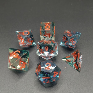 Peut inclure: Ensemble de sept dés polyédriques pour jeux de rôle. Les dés sont transparents avec des inclusions bleues et rouges, et des chiffres rouges. Comprend un D4, D6, D8, D10, D12, D20 et un dé de pourcentage.