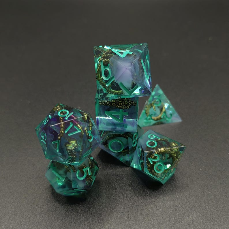 May include: A set of seven polyhedral dice made of translucent teal resin with purple swirls. Each die contains a miniature metallic bronze octopus figure inside, and the numbers are engraved and filled with bright teal paint.