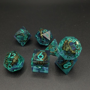 May include: A set of seven polyhedral dice made of translucent teal resin, each containing a metallic bronze-colored octopus tentacle figurine. The numbers are engraved in a bright teal color, clearly visible on the multifaceted surfaces.