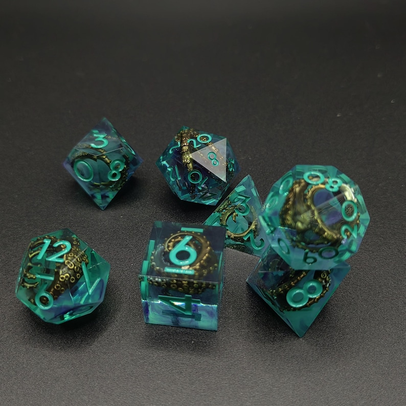 May include: A set of seven polyhedral dice made of translucent teal resin, each containing a metallic bronze-colored octopus tentacle figurine. The numbers are engraved in a bright teal color, clearly visible on the multifaceted surfaces.