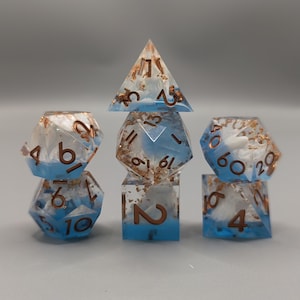 May include: A set of seven polyhedral dice for tabletop games. The dice are clear with a blue and white cloud-like design, copper-colored flecks, and copper-colored numbering. The set includes a d4, d6, d8, d10, d12, d20, and a percentile die.