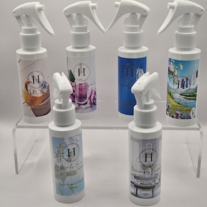 Puede incluir: Una colección de botellas de spray blancas con pulverizadores blancos. Cada botella tiene una etiqueta con el texto "Heavenly Scents" y varias imágenes. Las botellas están dispuestas en una pantalla transparente de varios niveles.