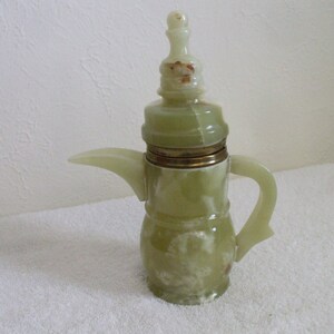 May include: A green and white ceramic teapot with a gold lid and a decorative top. The teapot has a spout and a handle.