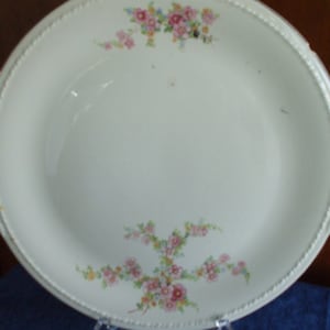 May include: A white ceramic serving platter with a floral design. The platter has a scalloped edge and a raised rim. The flowers are pink, yellow, and green.
