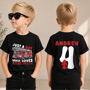 May include: A black short-sleeved t-shirt featuring a red fire truck graphic with the text "JUST A BOY WHO LOVES FIRE TRUCK" on the front and the name "ANDREW" above a large white number "4" and a red fire hydrant graphic on the back.