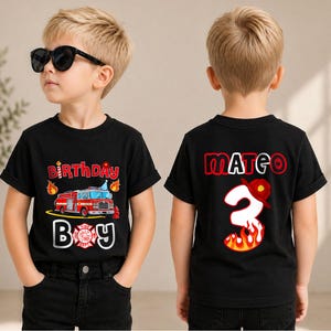 May include: A black short-sleeved t-shirt featuring a red fire truck graphic with the text Birthday Boy on the front and the name Mateo above a large number 3 decorated with flames and a firefighter helmet on the back of the garment.