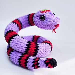 May include: A crocheted purple snake with black and red stripes. The snake has large, black eyes and a red tongue.