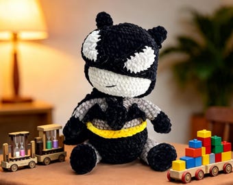 May include: A plush crochet doll featuring a black and white Batman-inspired design with a yellow belt, positioned between a wooden toy train carrying hourglasses and a wooden toy train carrying colorful stacked building blocks.