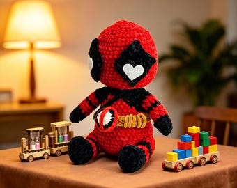 May include: A red and black crocheted plush doll featuring a mask with white heart-shaped eye patches and a gold belt with a circular buckle. The doll is positioned between a wooden toy train with hourglasses and a wooden train carrying colorful blocks.