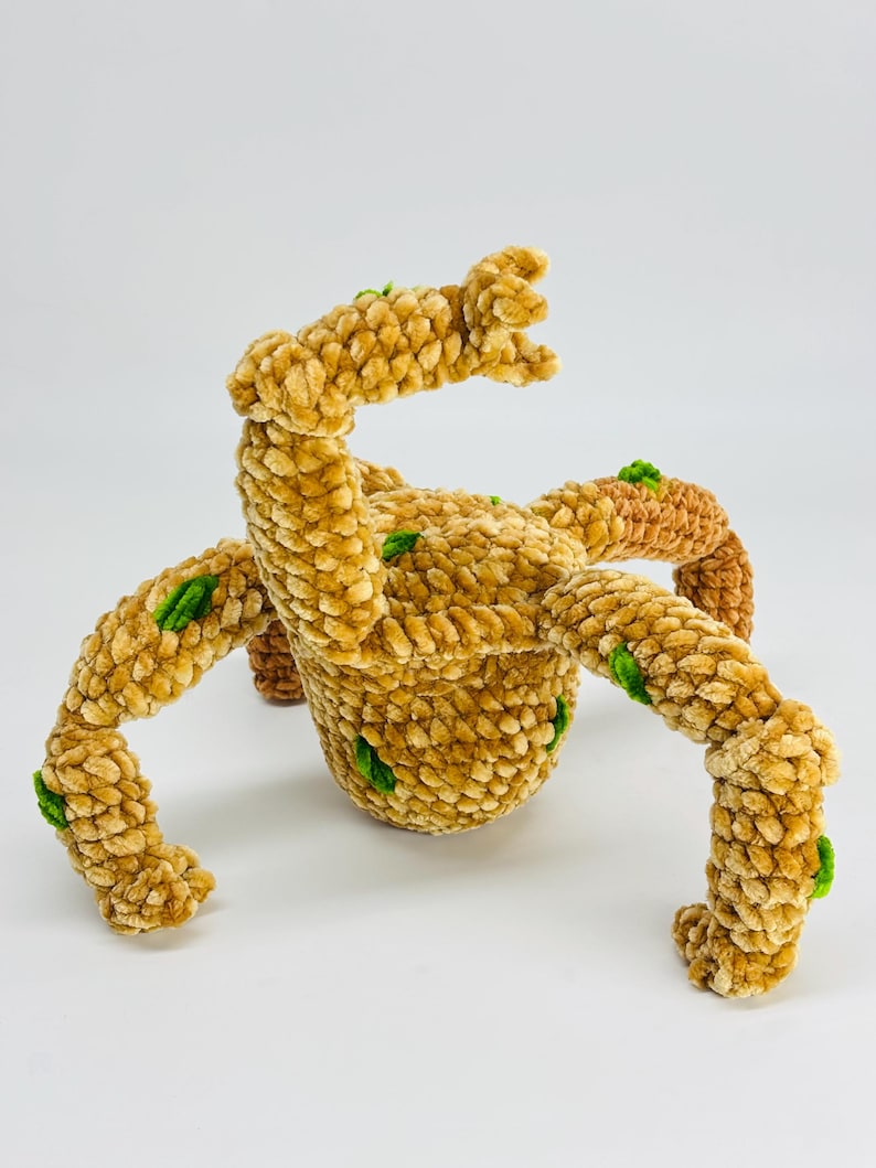 May include: A handmade, plush, tan-colored creature with multiple articulated limbs and a central body. The soft, textured toy features small green accents and is set against a white background. The toy is designed to resemble a fantastical creature.