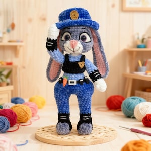 Puede incluir: Un conejo de peluche hecho a mano con uniforme de policía, que incluye un sombrero azul con una insignia dorada, un chaleco negro y pantalones azules. El conejo levanta su mano derecha en señal de saludo. Tiene orejas rosas y una zanahoria en el cinturón.