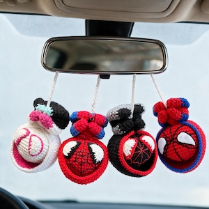 Può includere: Quattro ornamenti appesi all'uncinetto fissati allo specchietto retrovisore di un'auto. Ogni pezzo presenta un design a personaggio sferico con filato bianco, rosso, nero e blu, incluse maschere stilizzate con occhi bianchi e motivi a ragnatela.