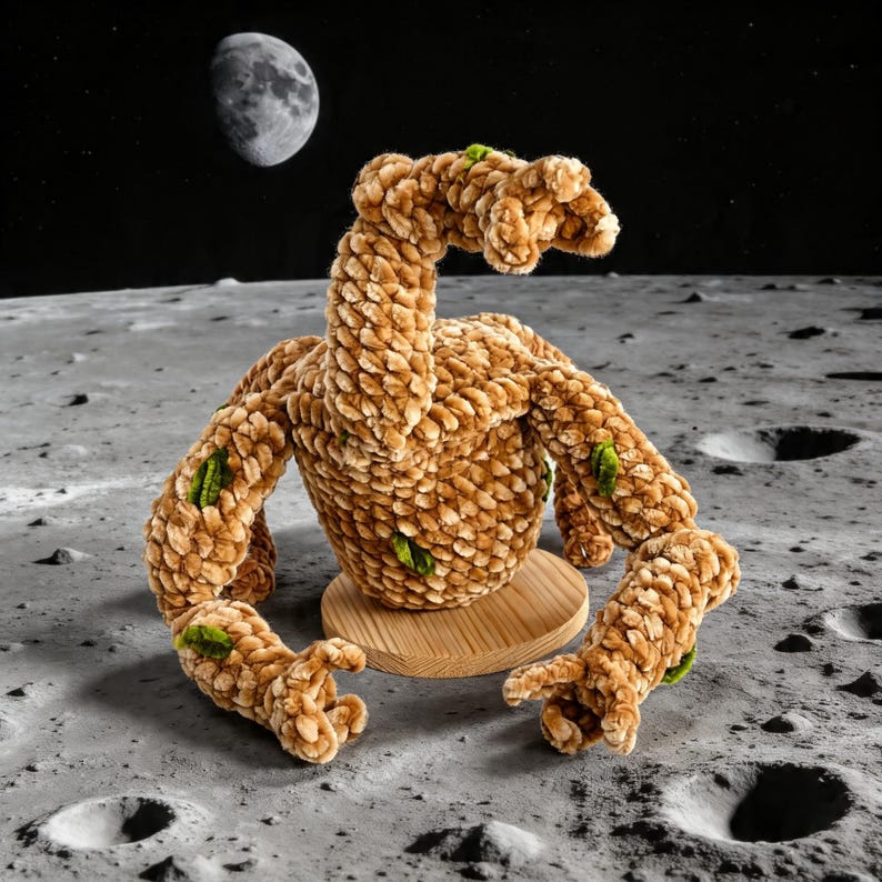 May include: A plush, tan-colored creature with a long neck and multiple limbs, accented with green patches, sits on a wooden base. The creature is set against a lunar landscape with the moon visible in the background.